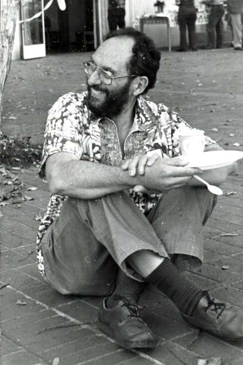 Sheldon Margen sitting on the ground, cross legged and smiling to his right